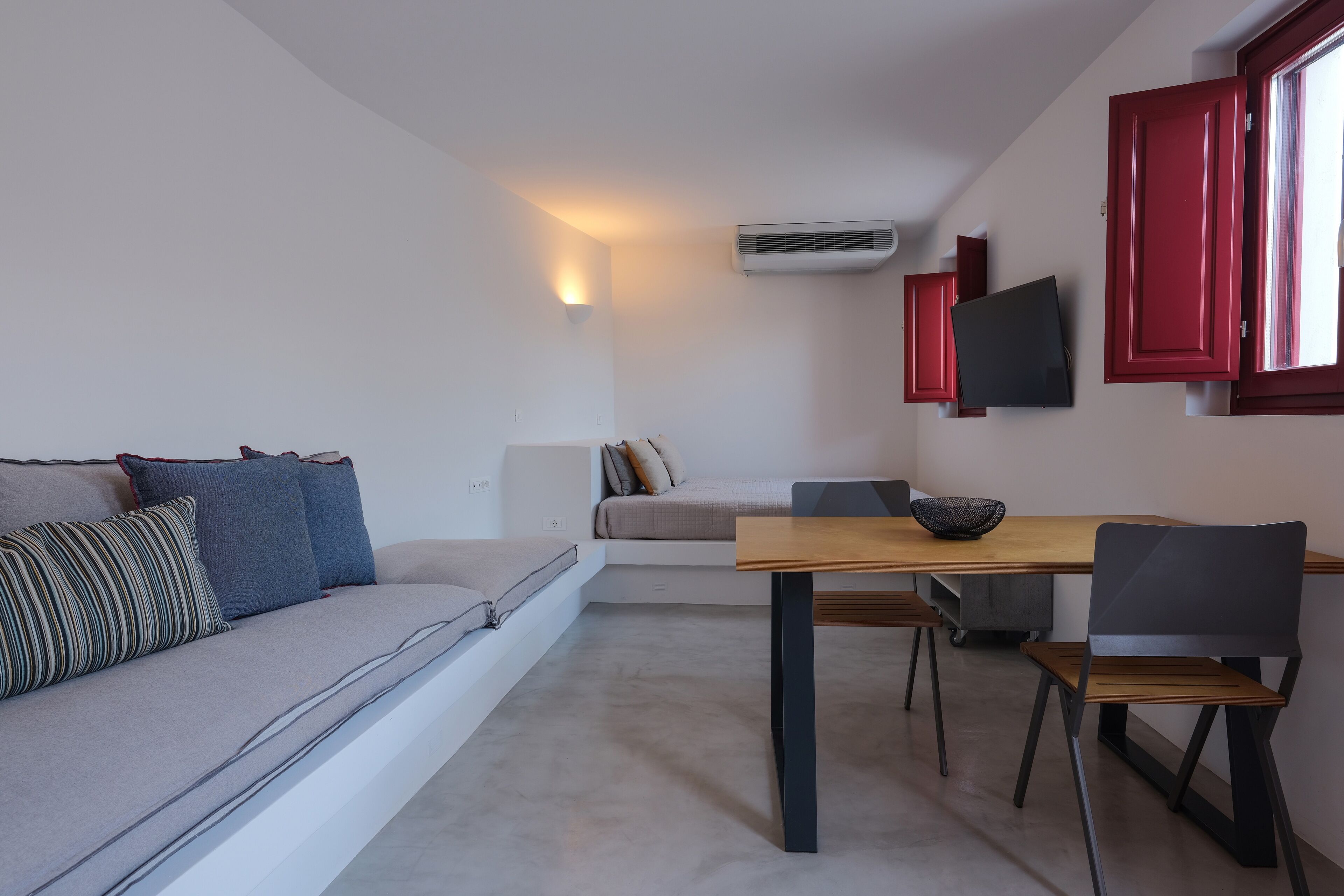 A modern living space with a sofa, a dining table, chairs, a TV, and a red-framed window.