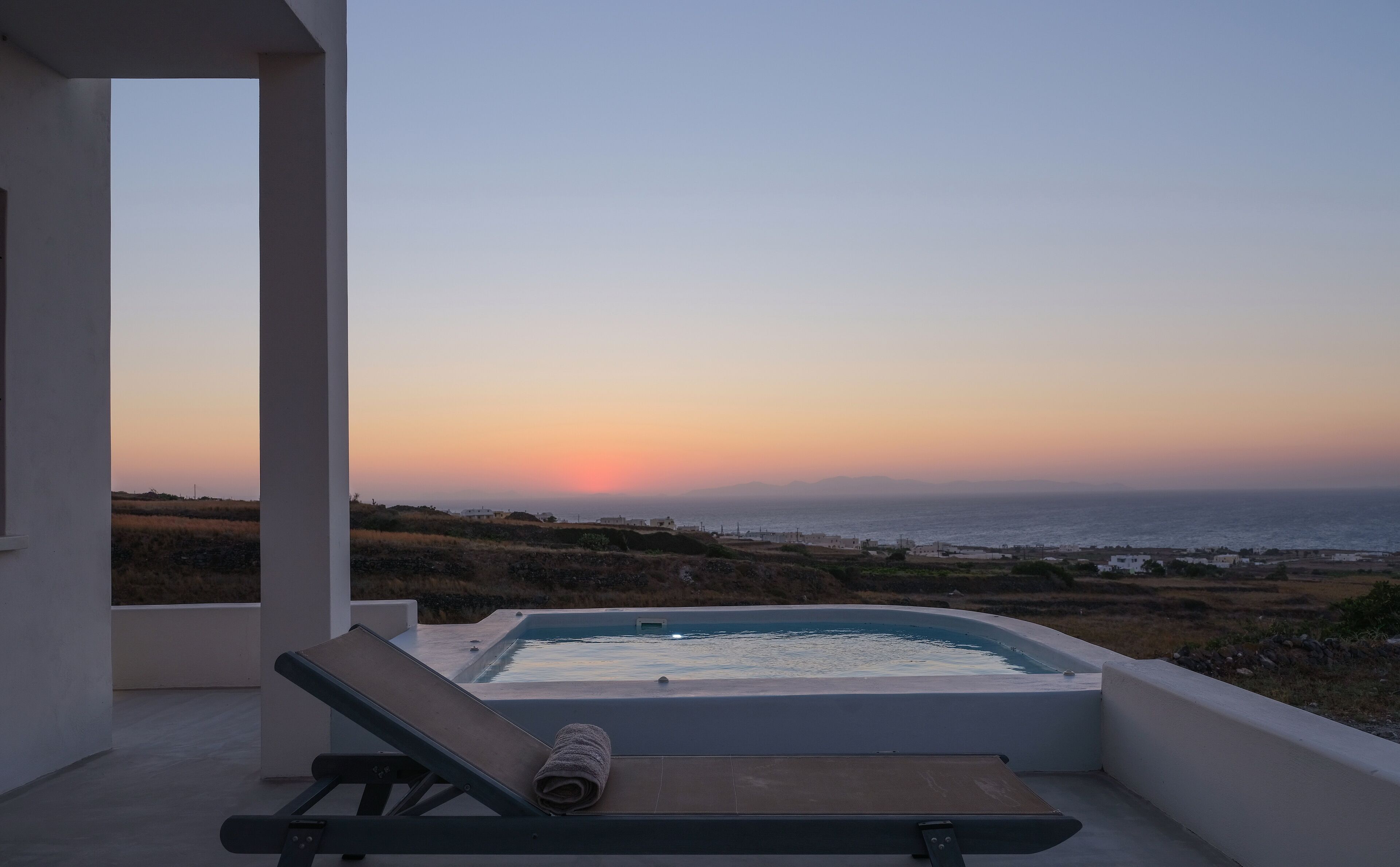 A balcony with a hot tub overlooking a coastal landscape during sunset.