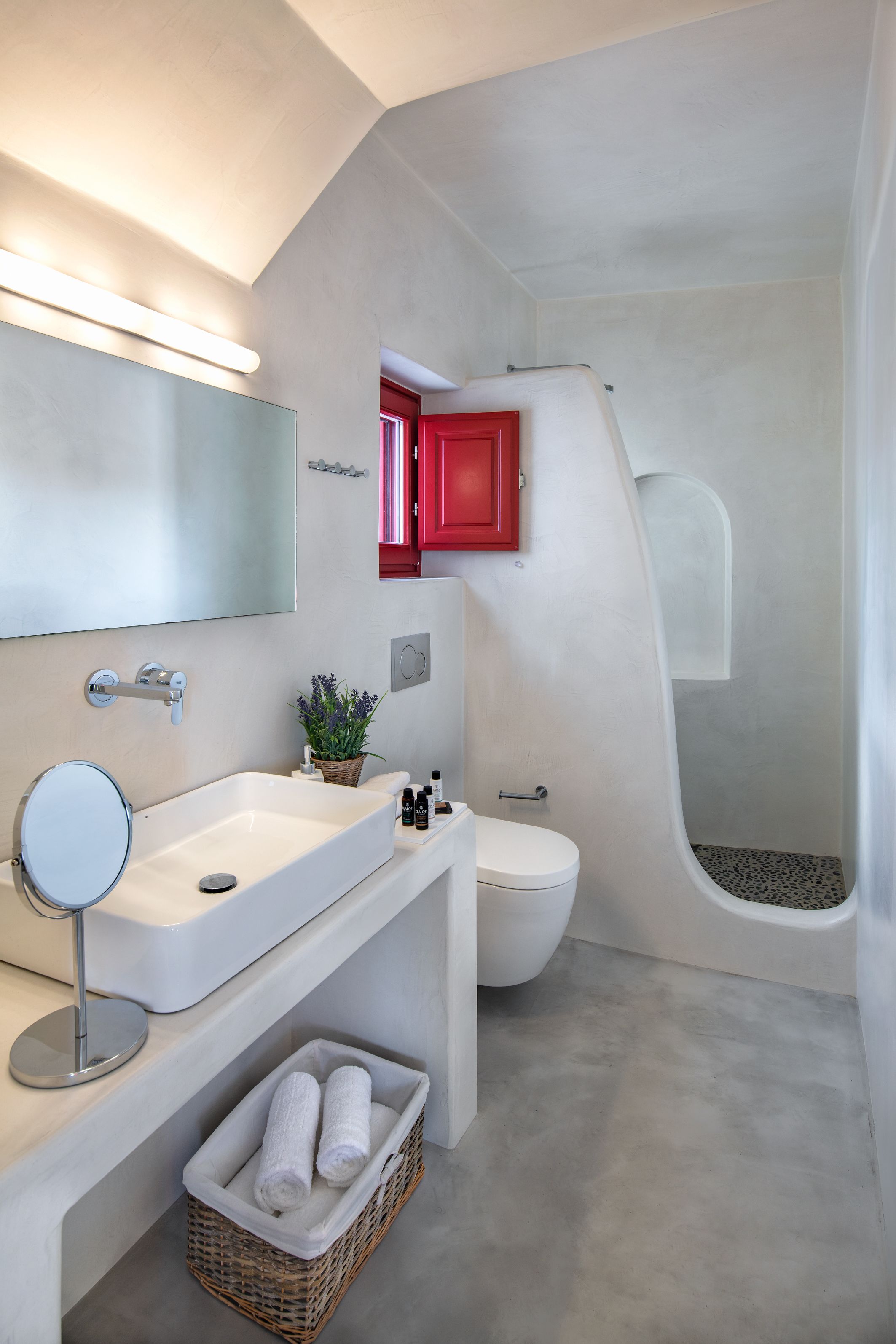 A modern bathroom with a white sink, mirror, and toilet, a red cabinet, and a shower area.