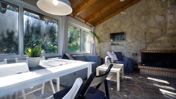 Una habitación revestida de piedra con chimenea, un televisor montado en la pared y un comedor con mesa y sillas.