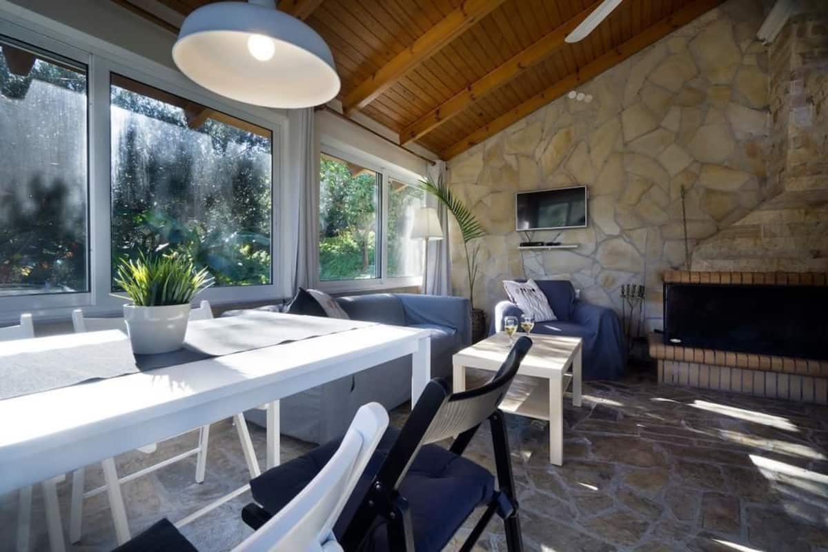 Une pièce aux murs recouverts de pierres, avec une cheminée, un téléviseur fixé au mur et un coin repas comprenant une table et des chaises.