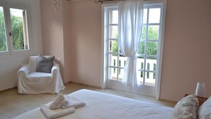 Un dormitorio con una cama grande, una silla, una ventana con cortinas y vistas a zonas verdes.