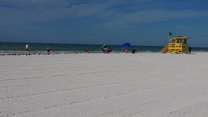A beach with a lifeguard tower, clear skies, and a few people.