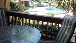 A glass-top table and a striped chair on a balcony overlooking a swimming pool with lounge chairs and palm trees. - 5 minutes drive to nr Siesta Key 1/1 Large condo. The pool heated (Sarasota)