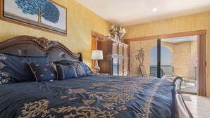 A bedroom with a large bed, a nightstand, a lamp, and a painting of a tree.