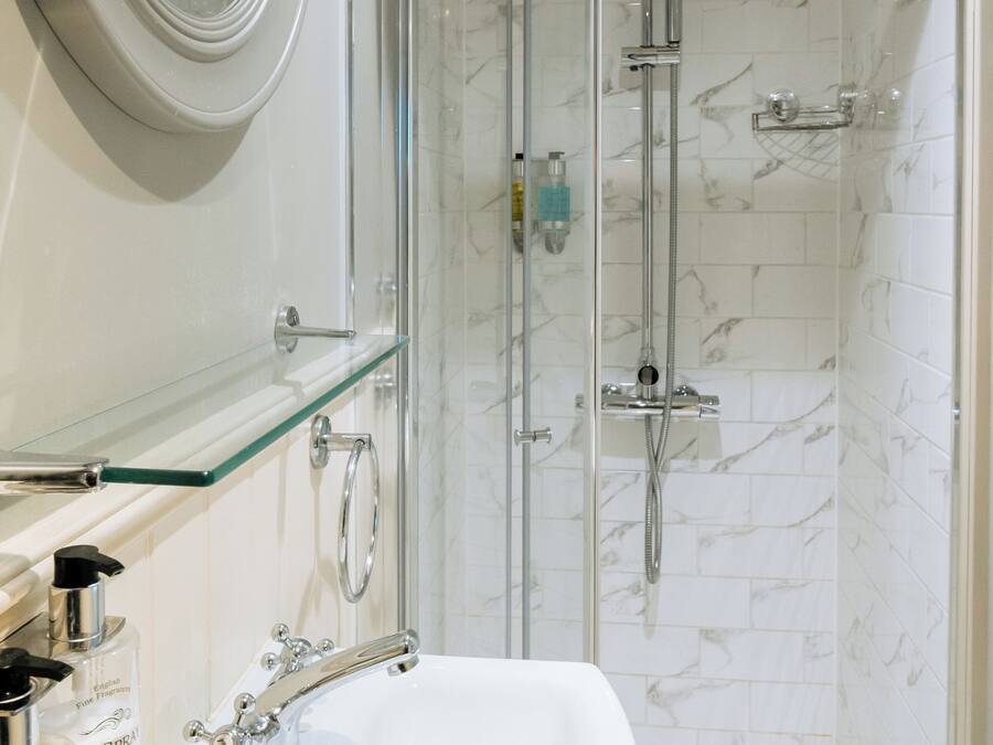 Un bagno moderno con doccia vetrata, lavandino bianco con un solo rubinetto e ripiano in vetro sopra il lavandino.