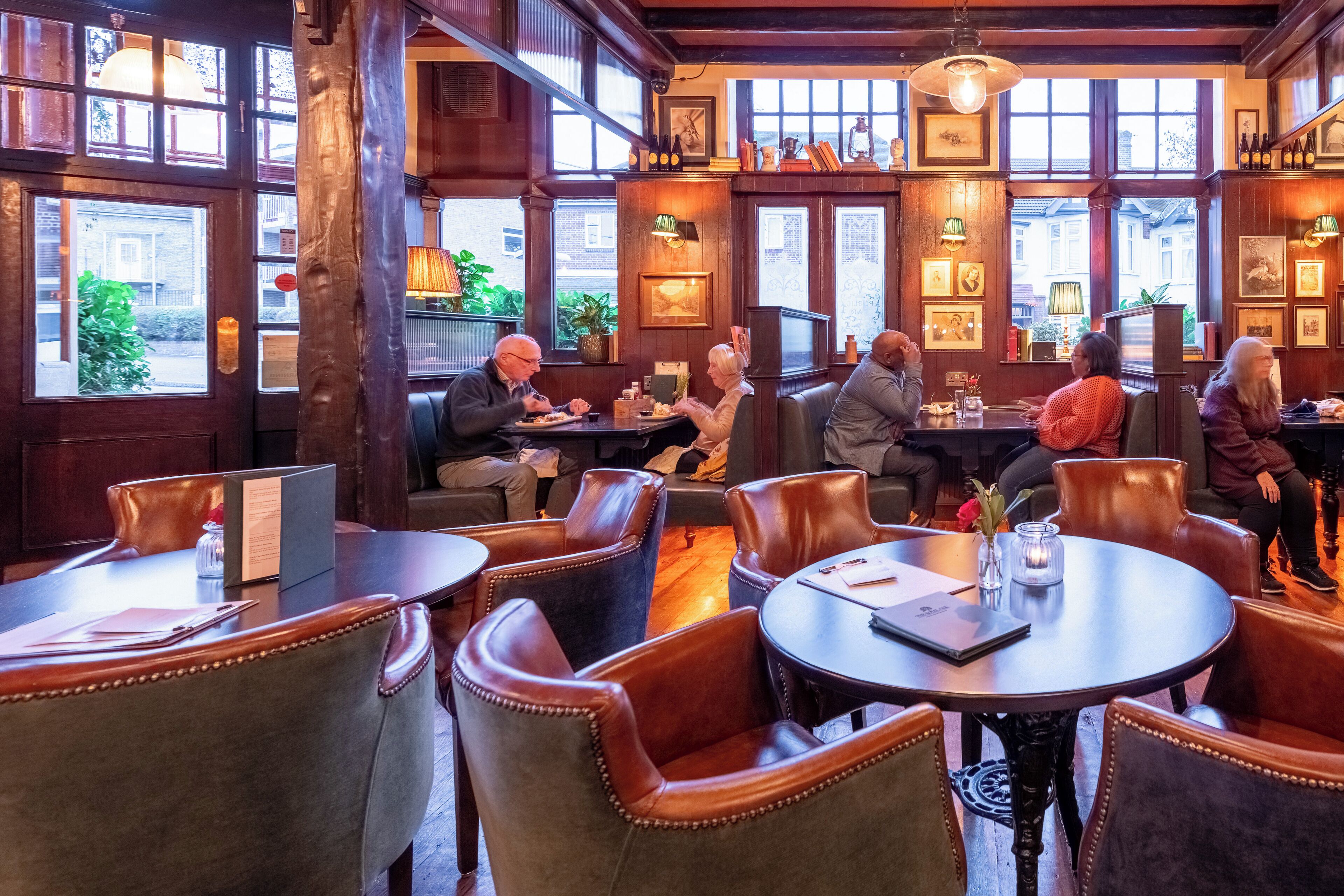 A cozy restaurant with wooden interiors, large windows, and leather chairs.