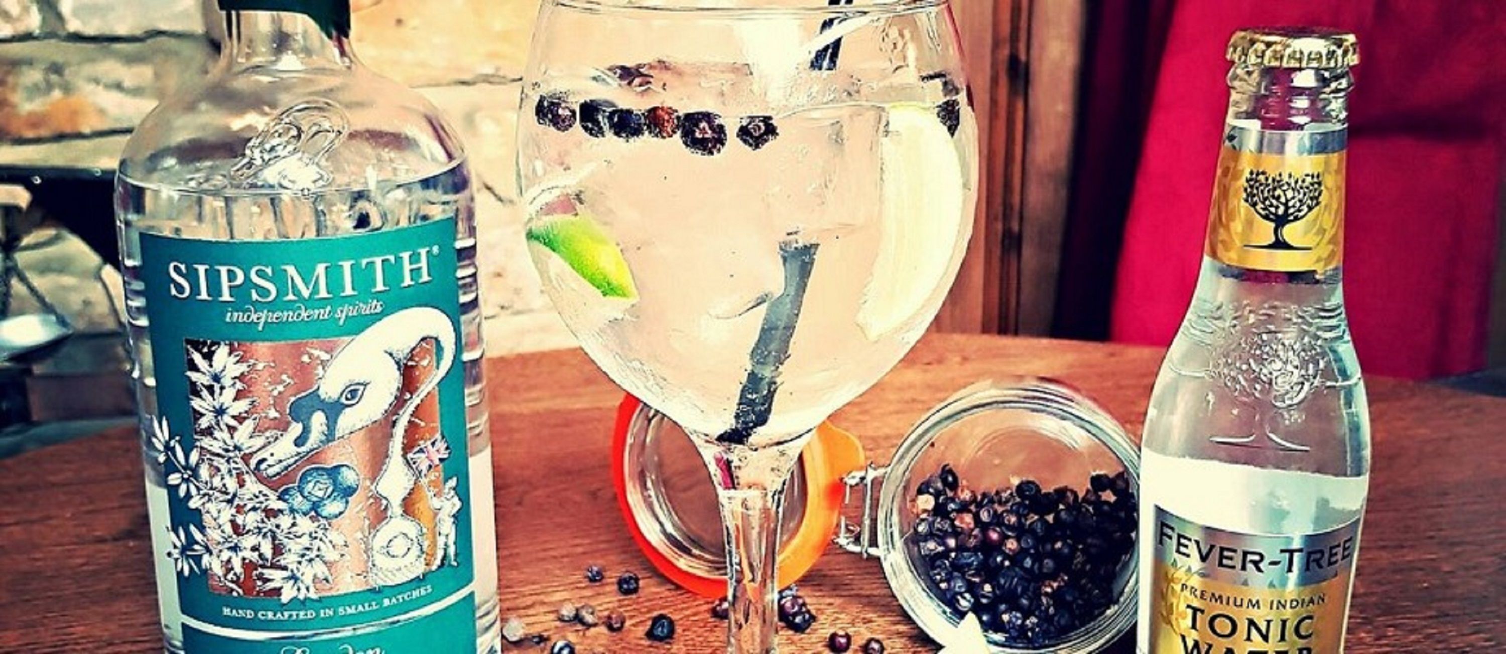 Une bouteille de gin Sipsmith, un verre contenant de l’eau tonique et une bouteille d’eau tonique Fever Tree, le tout posé sur une table en bois.