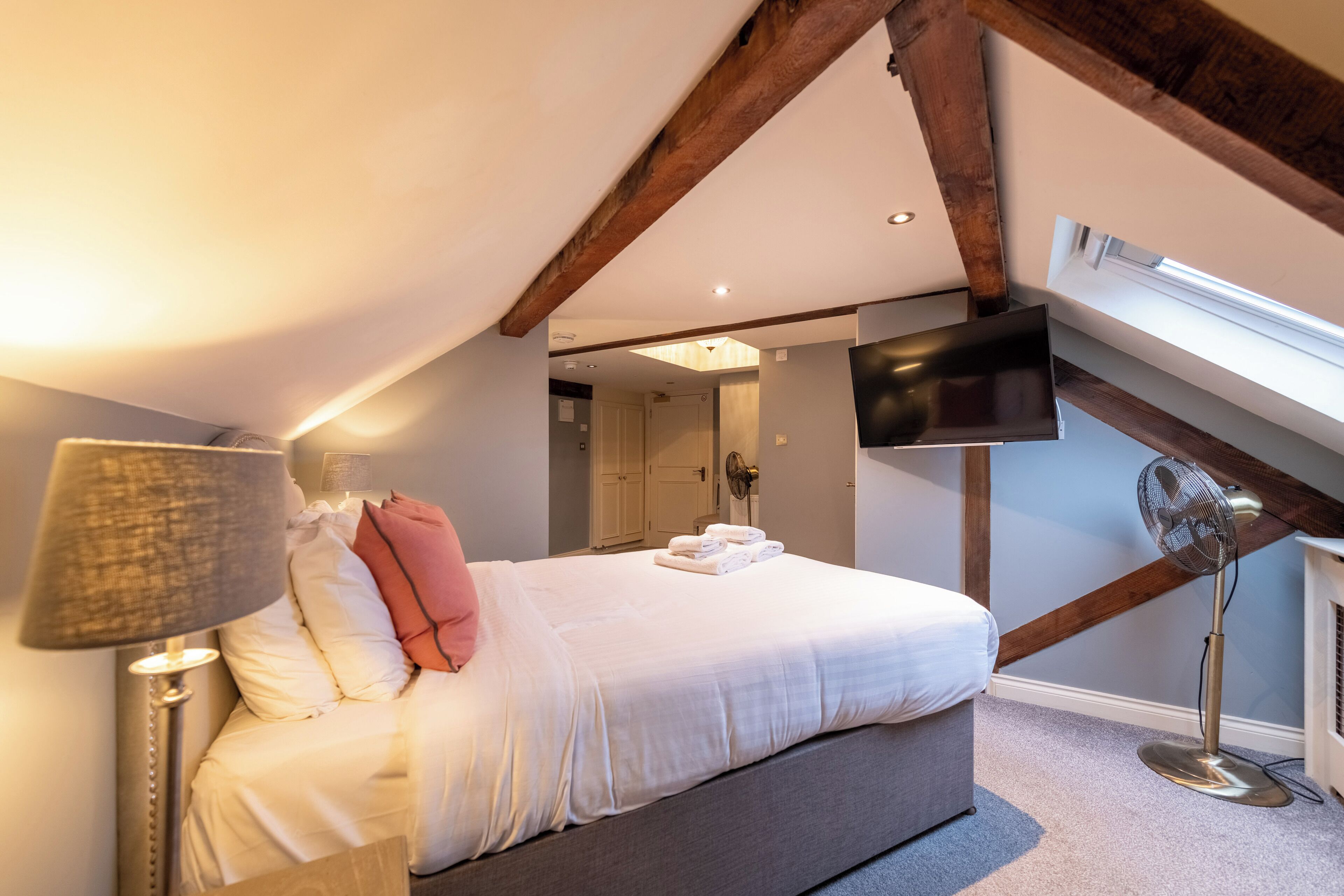 Un dormitorio con una cama, un ventilador de pie, un televisor montado en la pared y un ventilador de techo.
