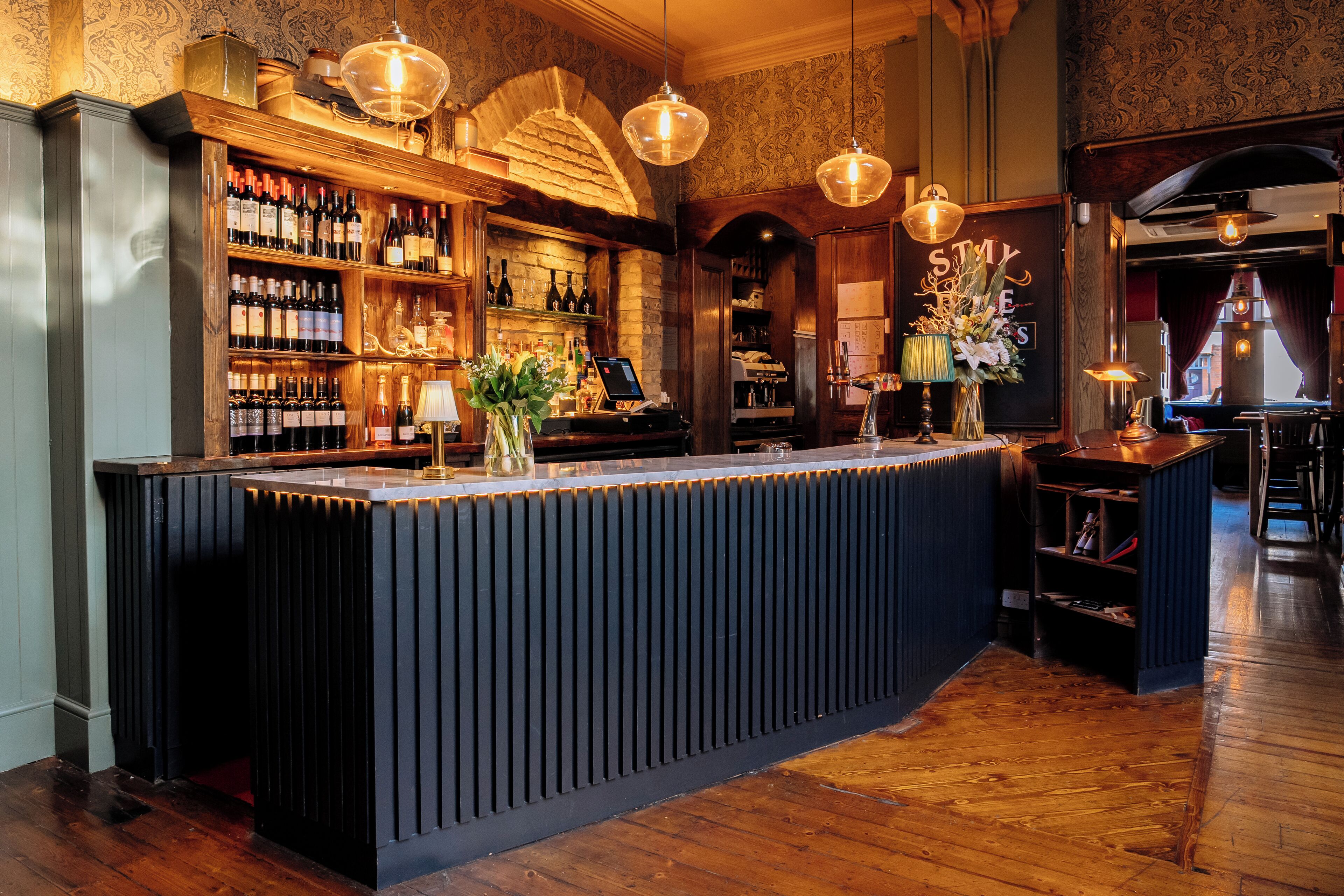 Een bar met een houten toonbank, flessenkasten en hangende lampen.