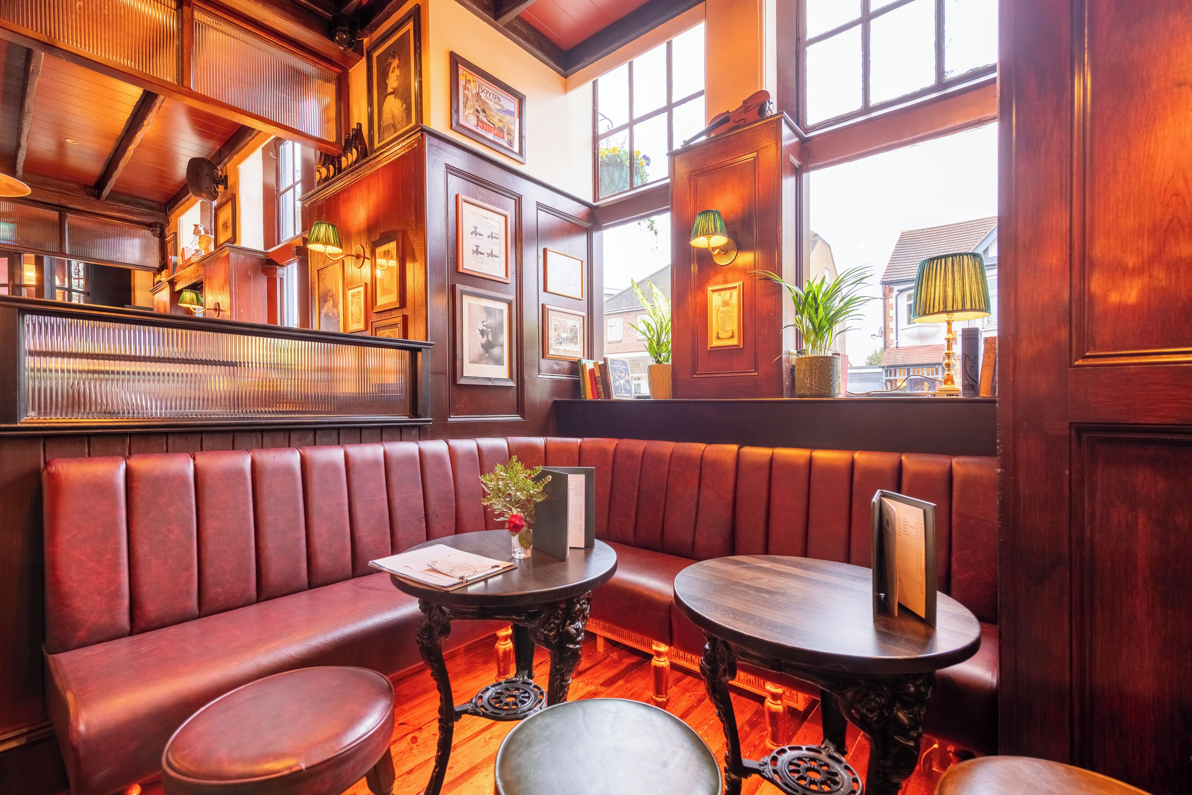 A cozy corner with a red leather booth, two round tables, and a wooden floor.