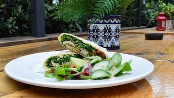Un plato con un wrap y ensalada sobre una mesa de madera, rodeado de macetas y un florero decorativo.