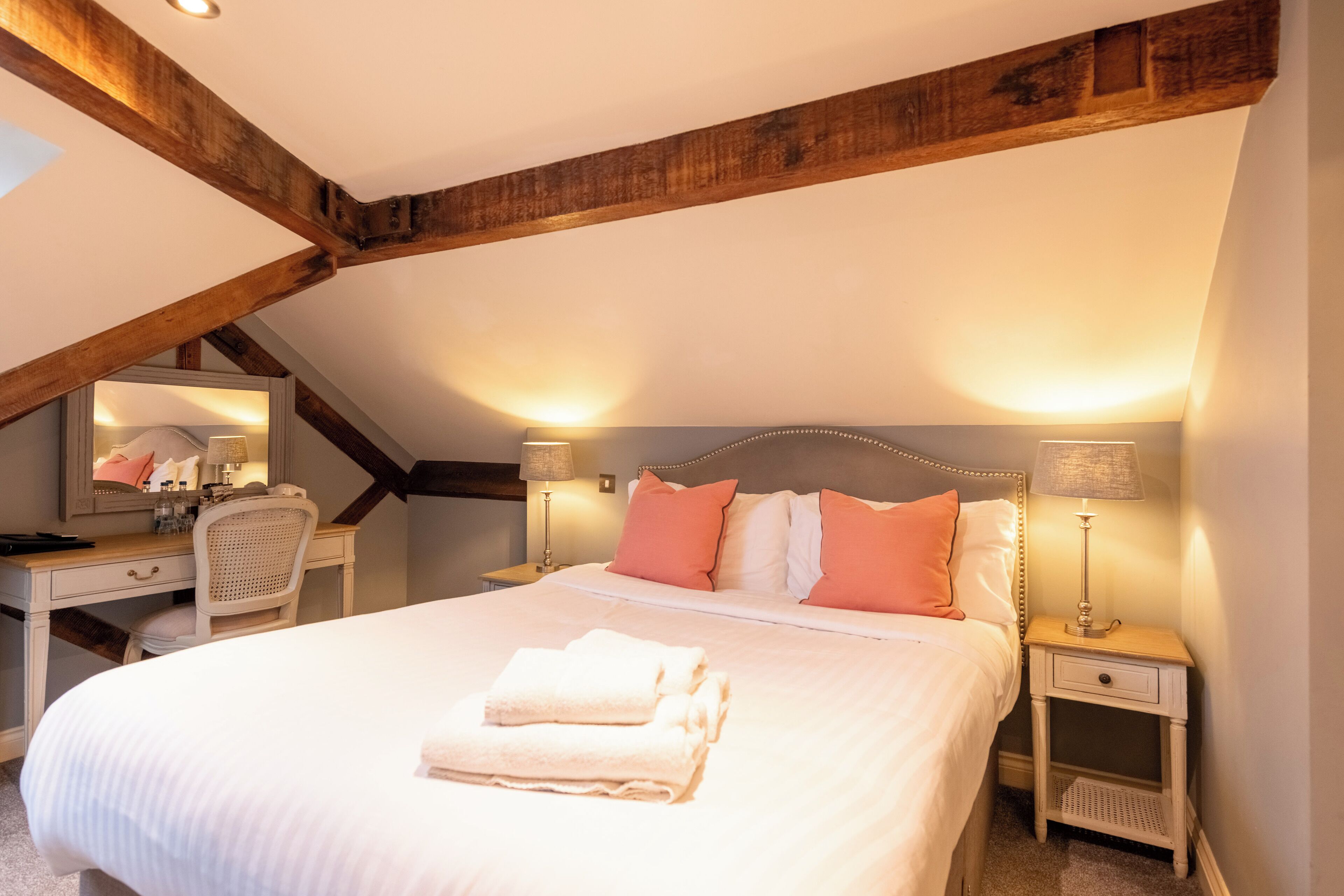 A bedroom with a large bed, two bedside tables, a desk with a chair, and a mirror.