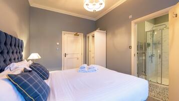 A hotel room with a large bed, a bedside lamp, a glass shower enclosure, and a door leading to another room.
