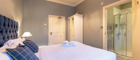A hotel room with a large bed, a bedside lamp, a glass shower enclosure, and a door leading to another room.