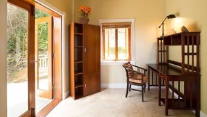 Quarto com estante de madeira, escrivaninha com abajur, cadeira e janela com cortinas.
