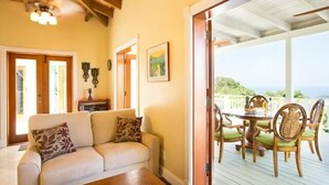 Uma sala de estar acolhedora com sofá, mesa de jantar e cadeiras, ventilador de teto e vista para o exterior.