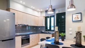 A modern kitchen with a stainless steel refrigerator, wooden cabinets, a tiled backsplash, and a dining area with a white table and black chairs. - Toroni Blue (Sithonia)