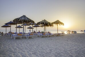 A beach with rows of sun loungers and thatched umbrellas.