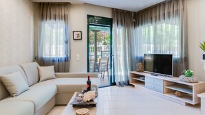 A modern living room with a sectional sofa, a flat-screen TV, and a dining area visible through a glass door. - Toroni Blue (Sithonia)