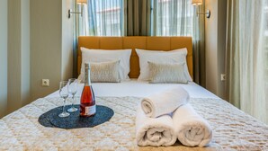 A neatly made bed with a rolled towel, two wine glasses, and a bottle on a textured bedspread. - Toroni Blue (Sithonia)
