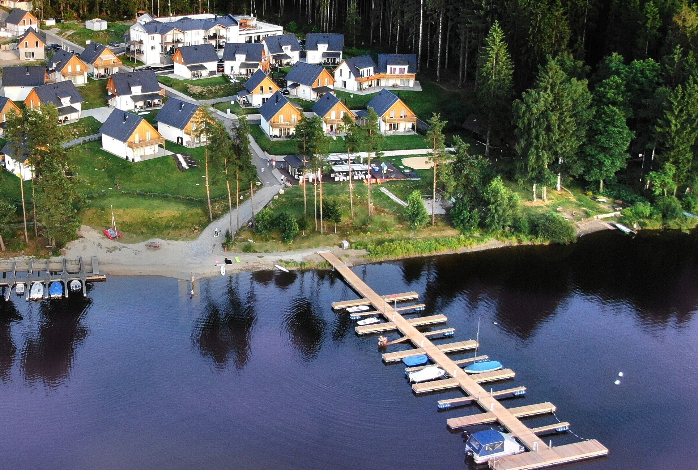 Vue aérienne d’un quartier résidentiel au bord d’un lac, avec des maisons, un quai et des bateaux.