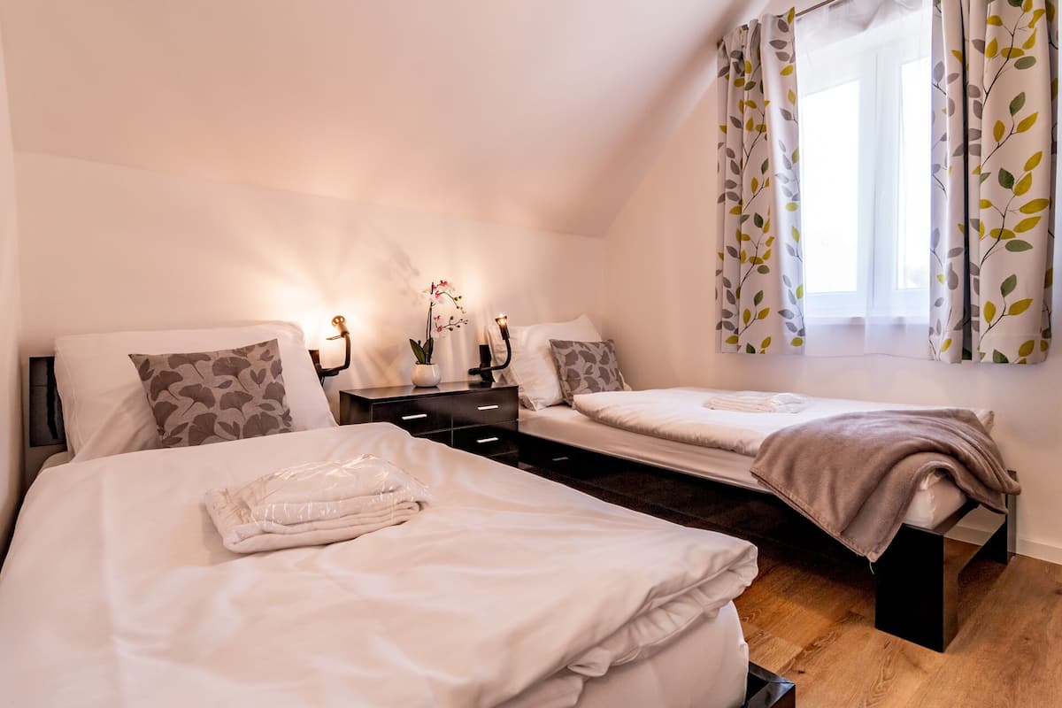 A bedroom with two beds, a nightstand, a lamp, and a window with leaf-patterned curtains.