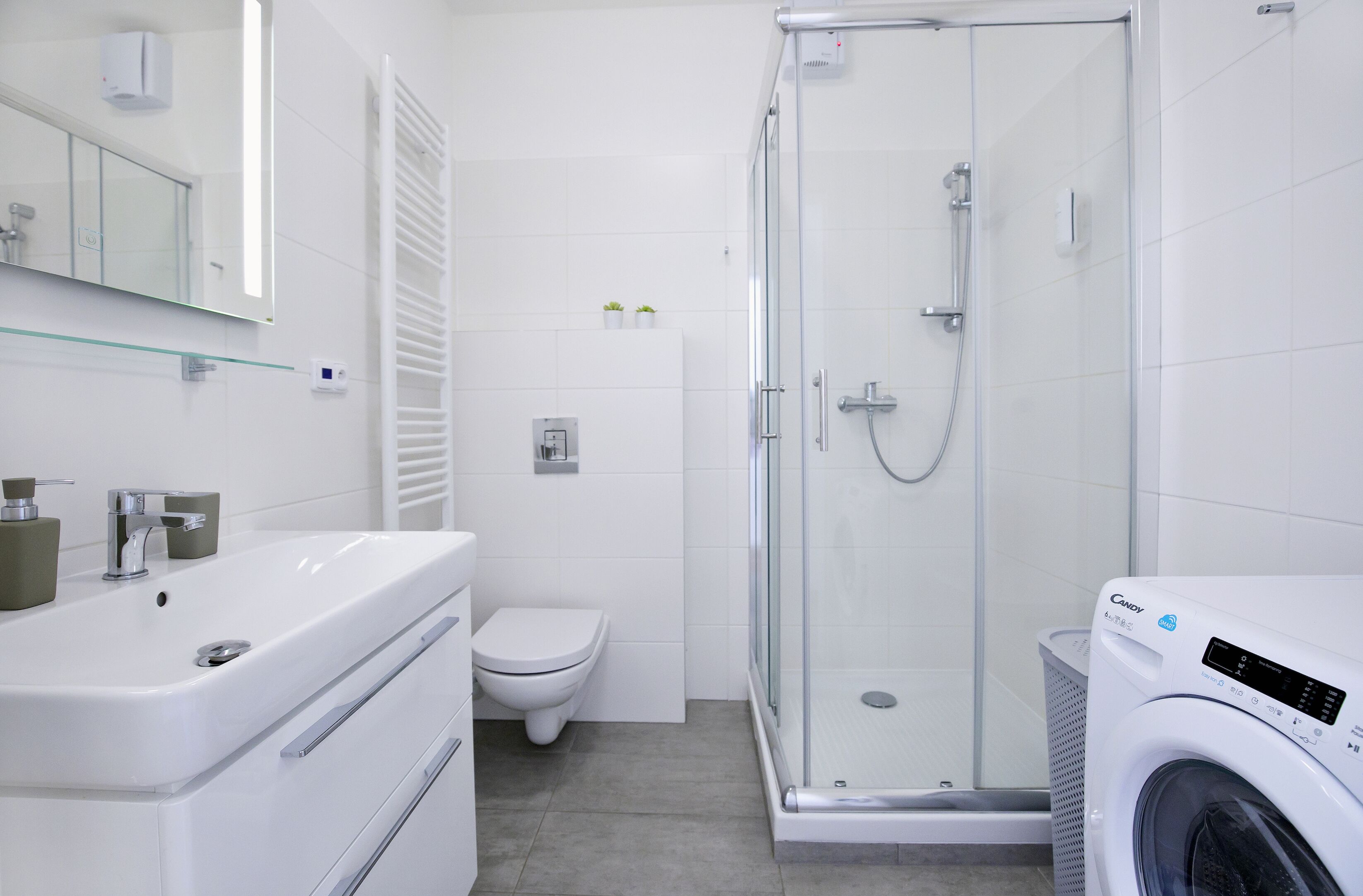 Un baño moderno con ducha de vidrio, lavamanos blanco y lavadora integrada.