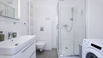 Un baño moderno con ducha de vidrio, lavamanos blanco y lavadora integrada.