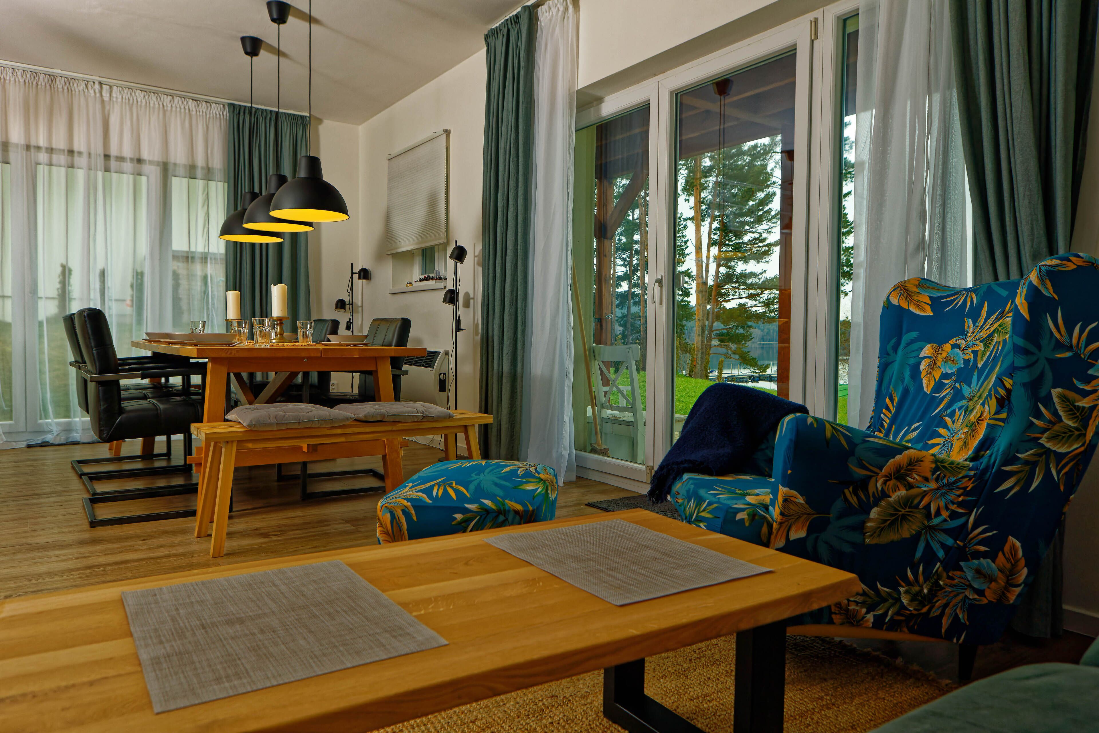 Un salon moderne avec une table à manger en bois, deux fauteuils bleus, un canapé et une grande fenêtre avec des rideaux.