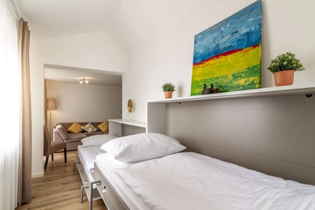 A hotel room with a bed, a desk, a chair, a sofa, and a colorful painting on the wall.