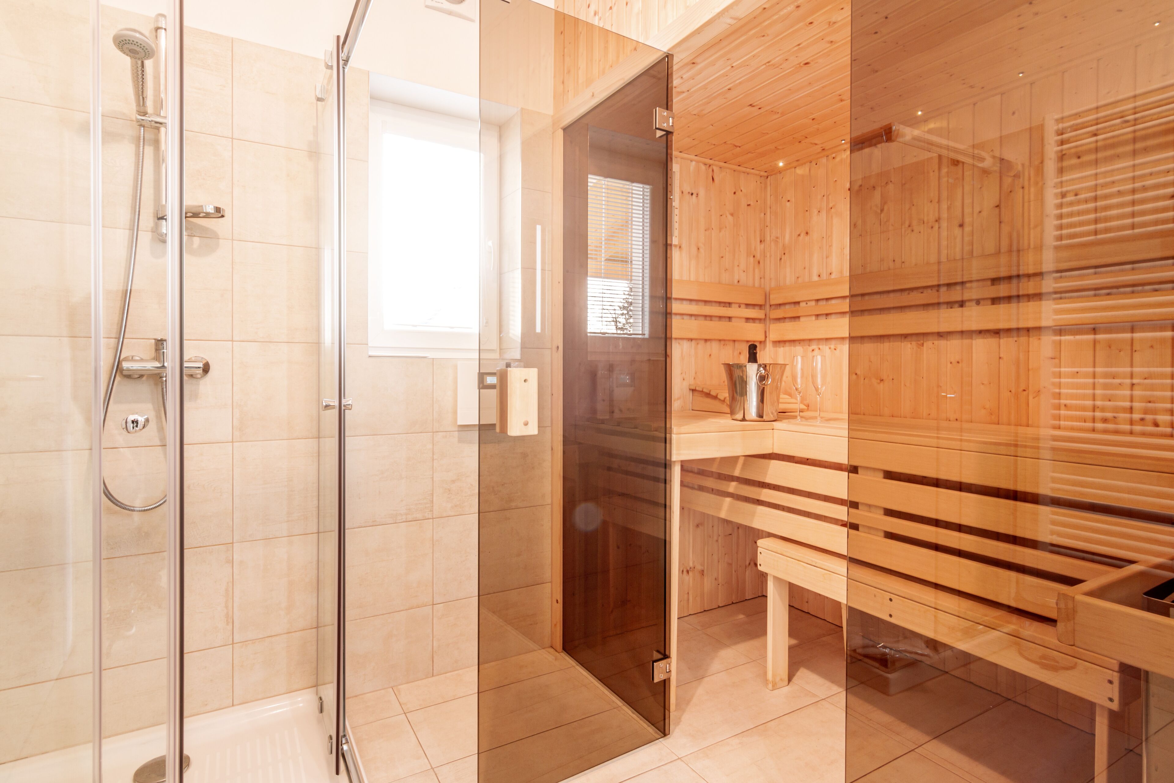 Een moderne badkamer met een glazen douchecabine, houten sauna banken en een zichtbaar raam.