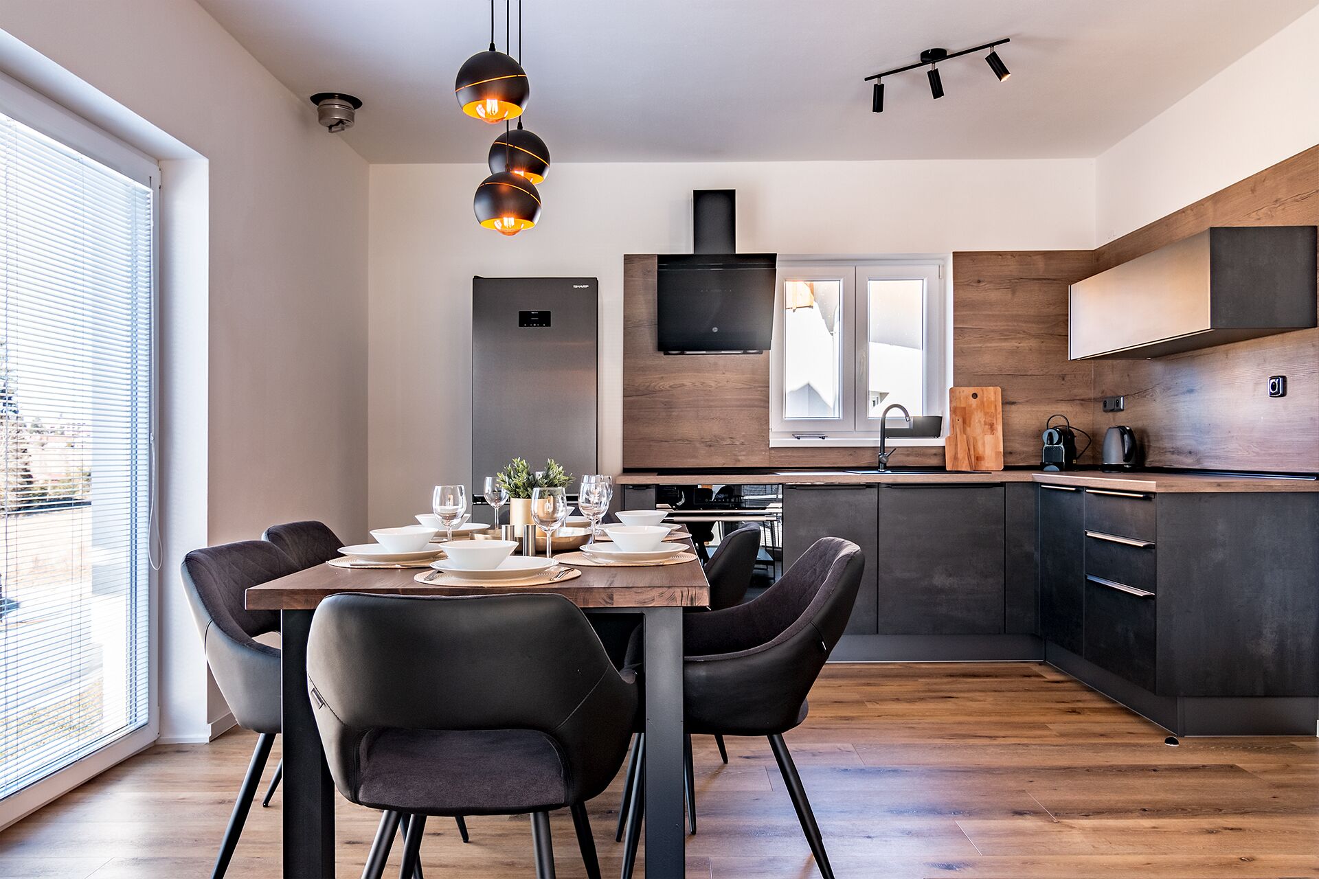 A modern kitchen with dark cabinetry, a wooden dining table, and black chairs.