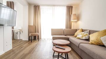 Ein modernes Wohnzimmer mit einer Couch, zwei runden Tischen, einem Fernseher und einer Lampe.