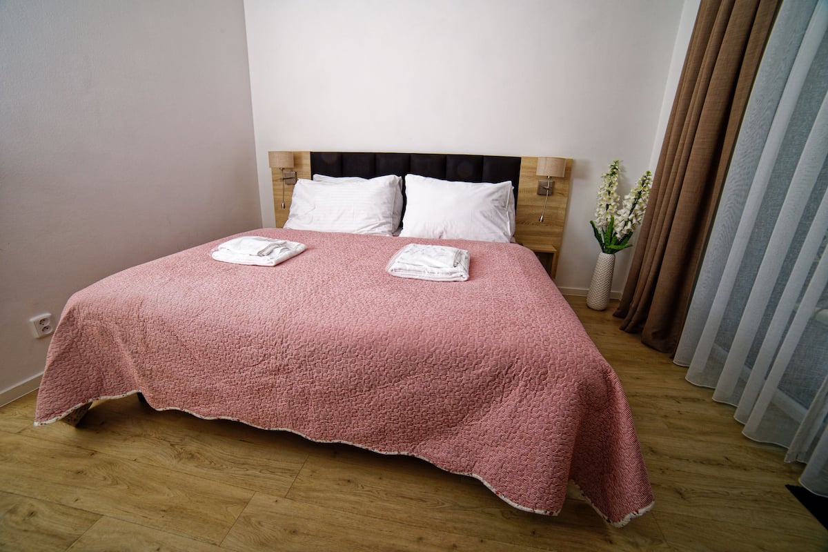A neatly made bed with a pink blanket, white pillows, and a wooden headboard.