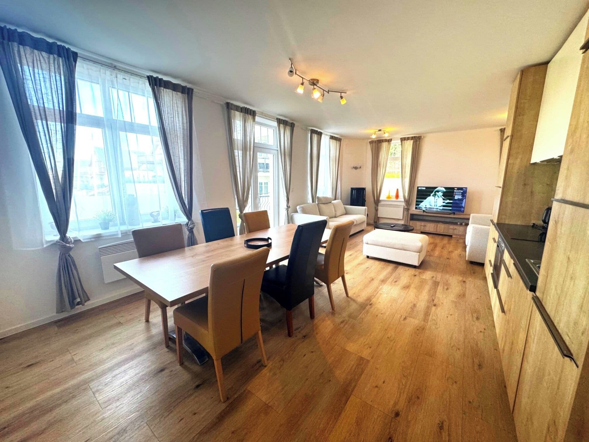 A modern living room with a dining area, wooden flooring, and a flat-screen TV.