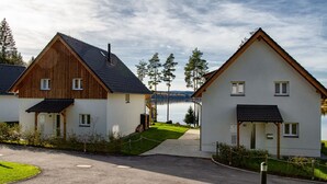 Two modern houses with a paved driveway leading to a body of water, surrounded by greenery and trees. - Lakeside Village Větrník (Frymburk)