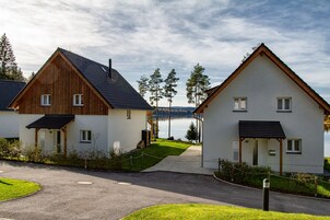 Dos casas modernas con un camino de entrada pavimentado que conduce a una masa de agua, rodeado de follaje y árboles.