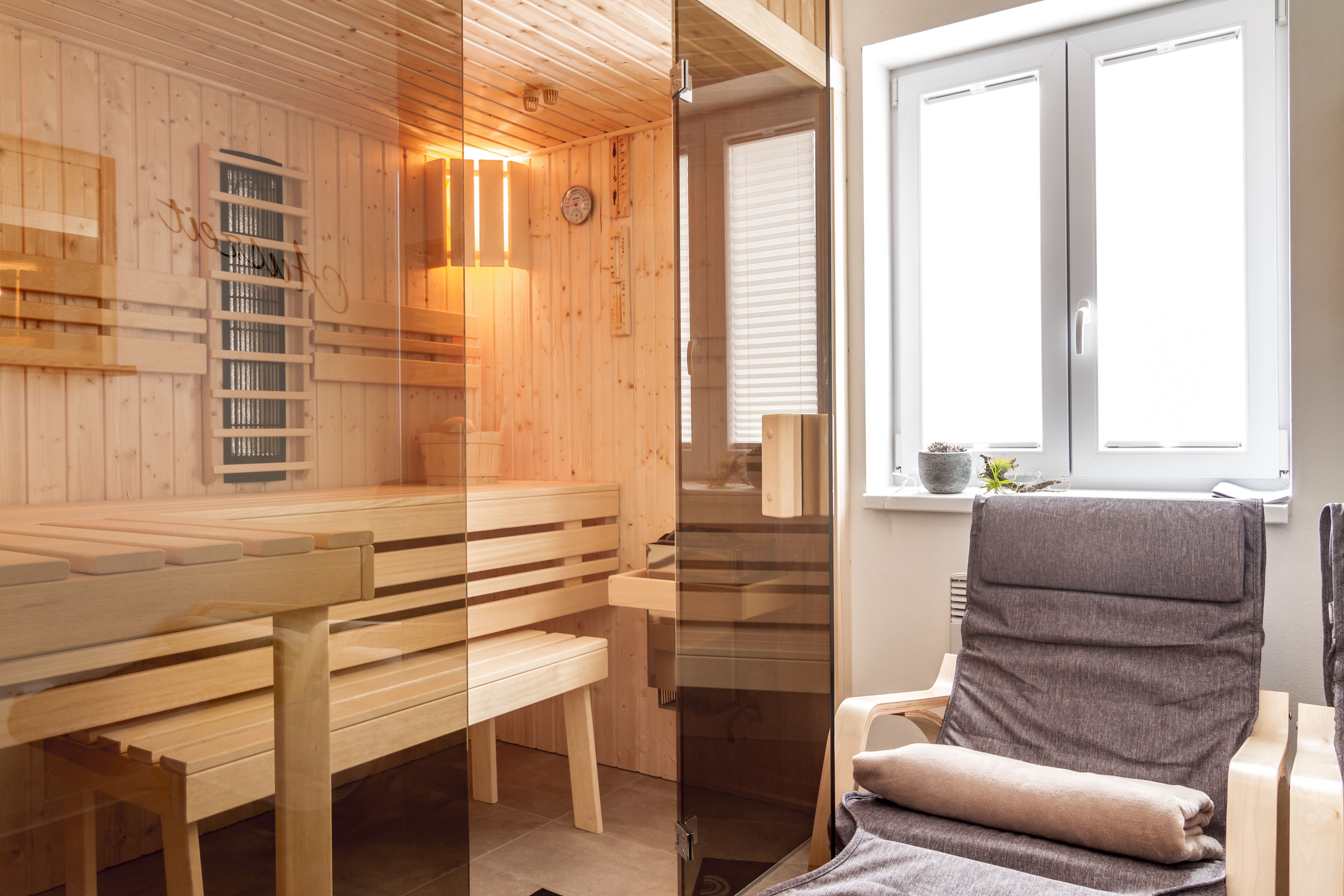 Sala de sauna con bancos de madera y una puerta de vidrio que da a una ventana.