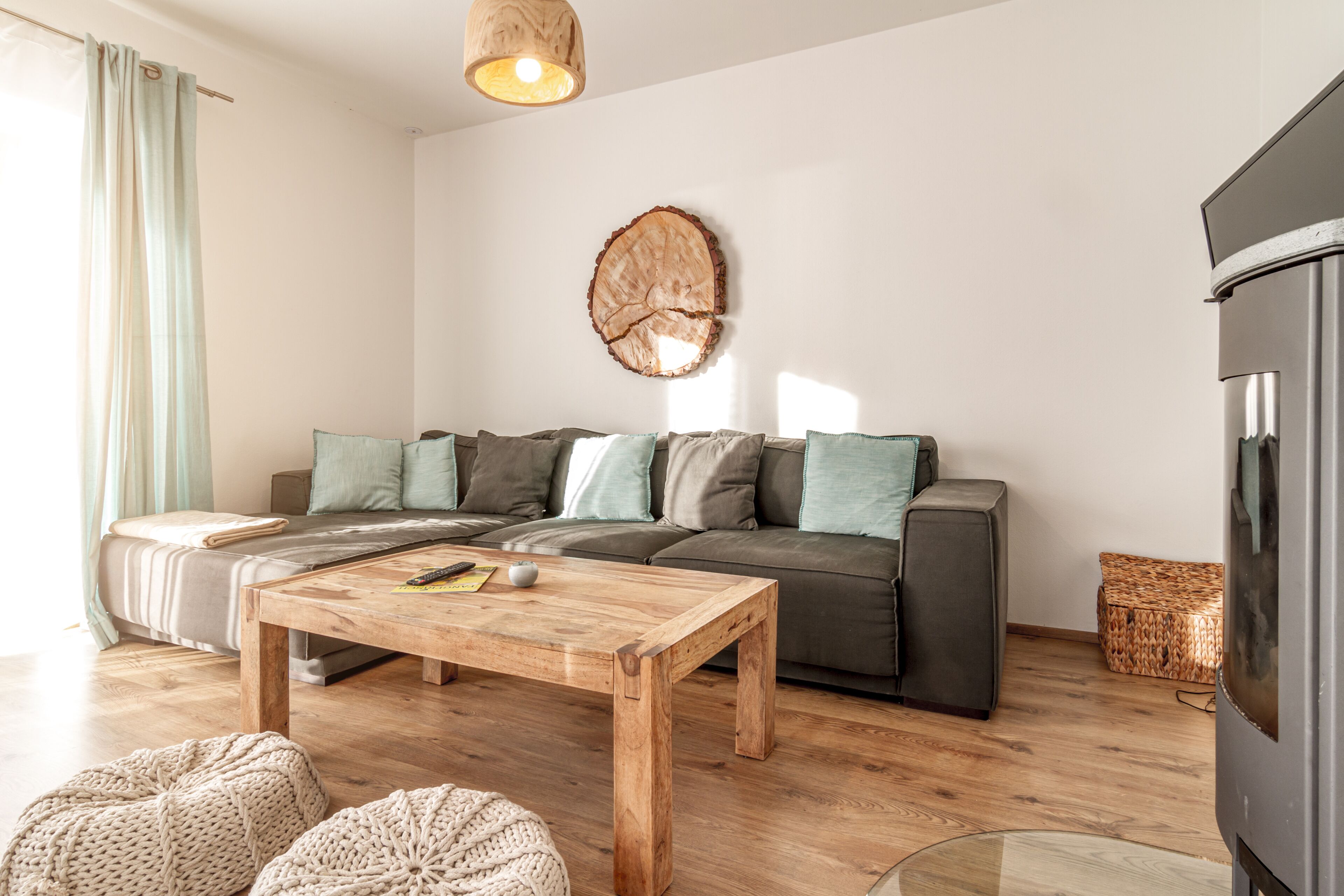 A modern living room with a wooden coffee table, a sofa with cushions, a large wooden log wall decoration, and a refrigerator.