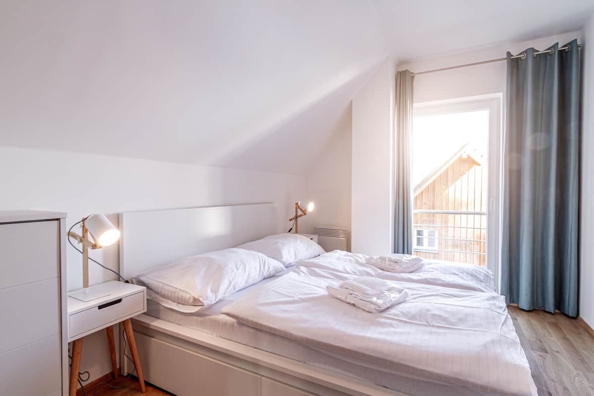A bedroom with a bed, bedside lamps, a nightstand, and a window with curtains.