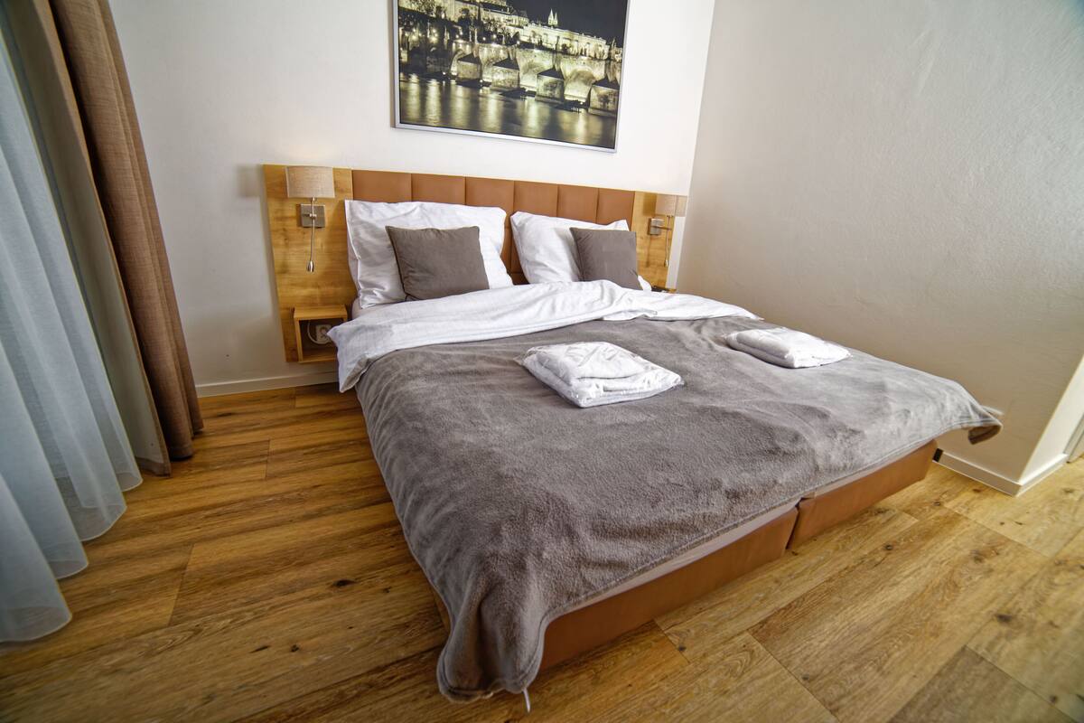 A neatly made bed with a wooden headboard, a large framed picture above it, and a wooden floor.