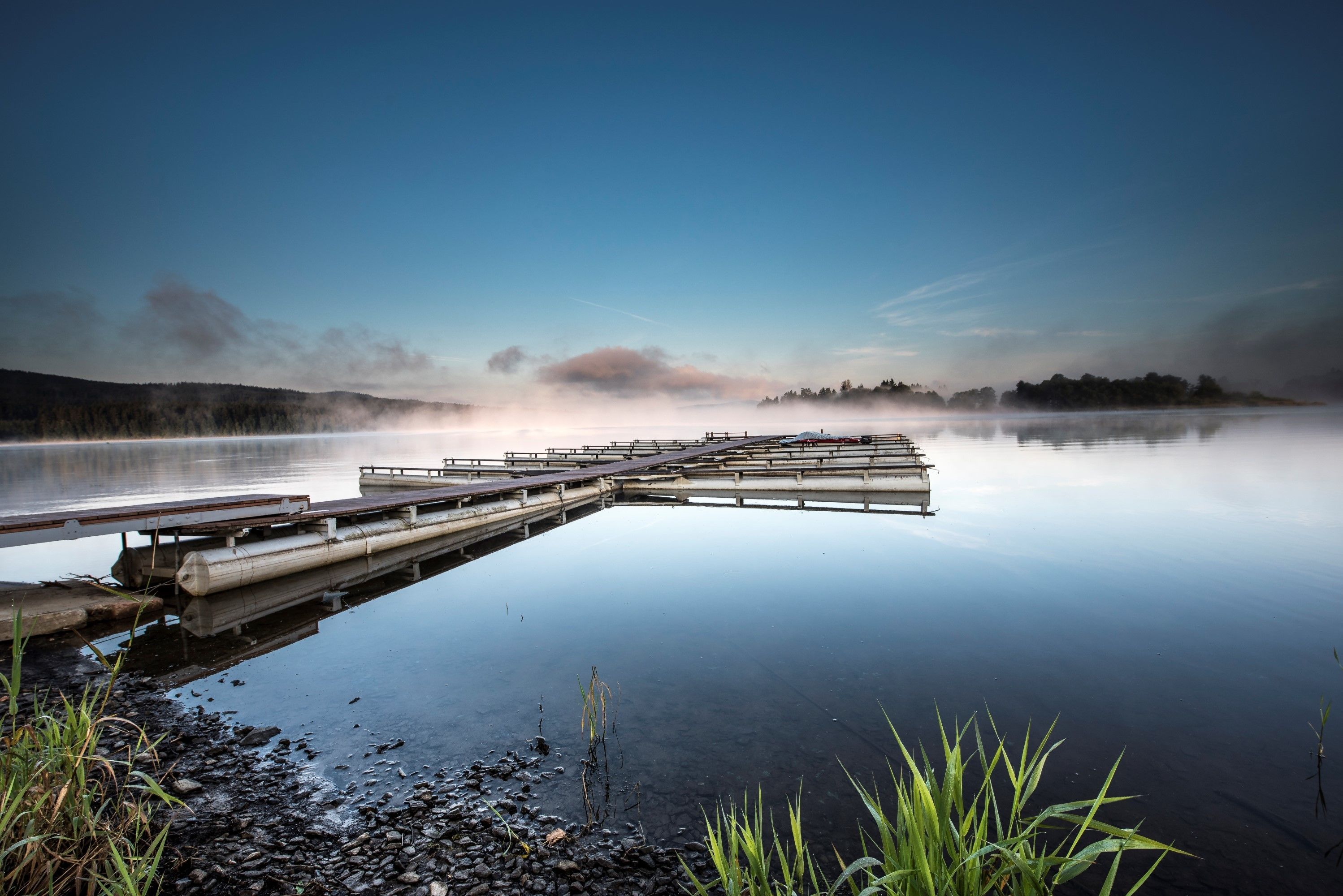 Un lago tranquilo con un muelle de madera que se adentra en el agua, rodeado de aguas serenas y vegetación.