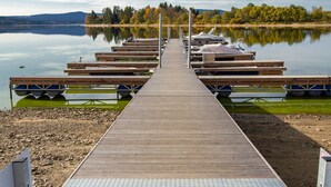 A wooden dock leading to a row of boats on calm water, surrounded by trees and hills. - Lakeside Village Větrník (Frymburk)