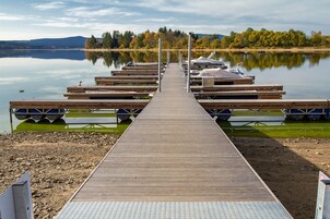 Un muelle de madera que conduce a una hilera de barcos en aguas tranquilas, rodeado de árboles y colinas.
