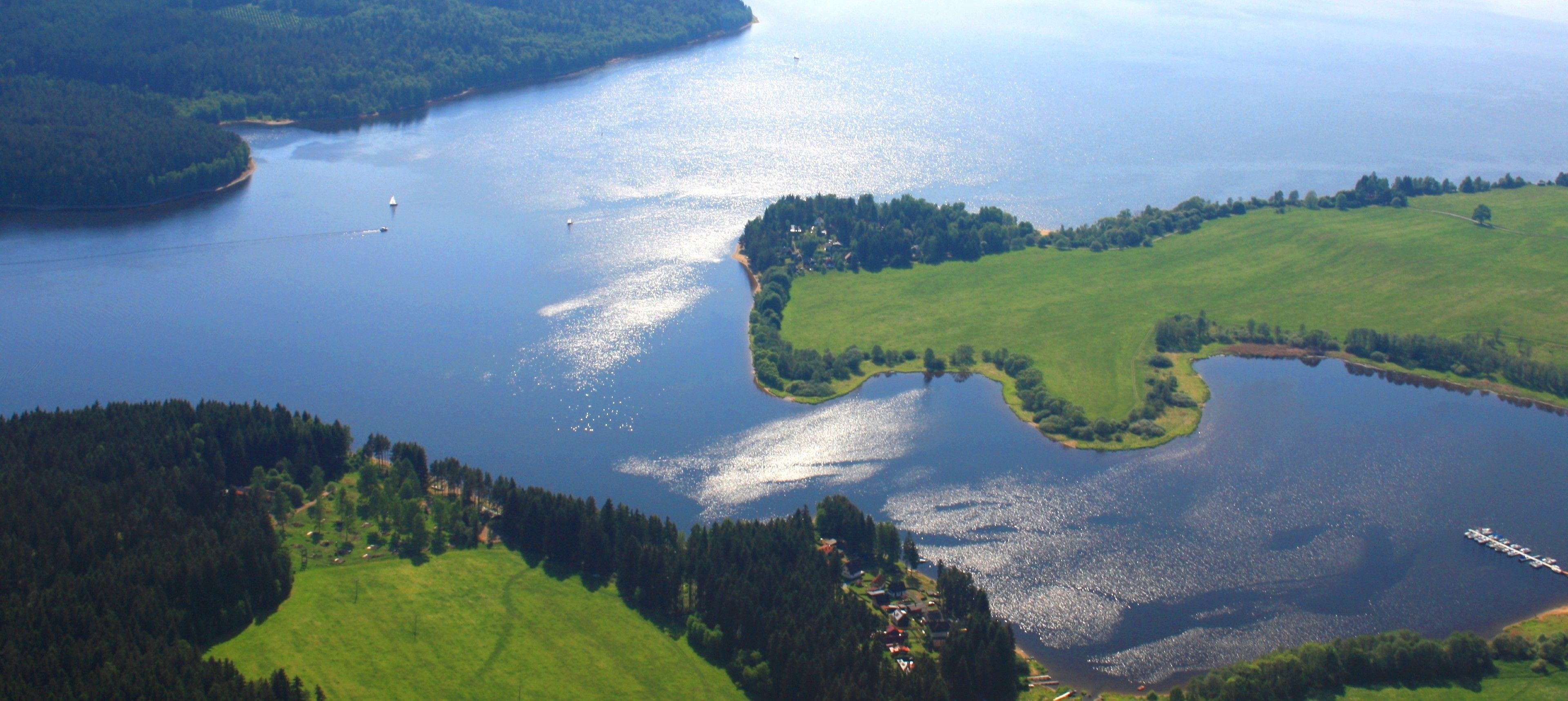 An aerial view of a lake surrounded by green fields and forested areas.