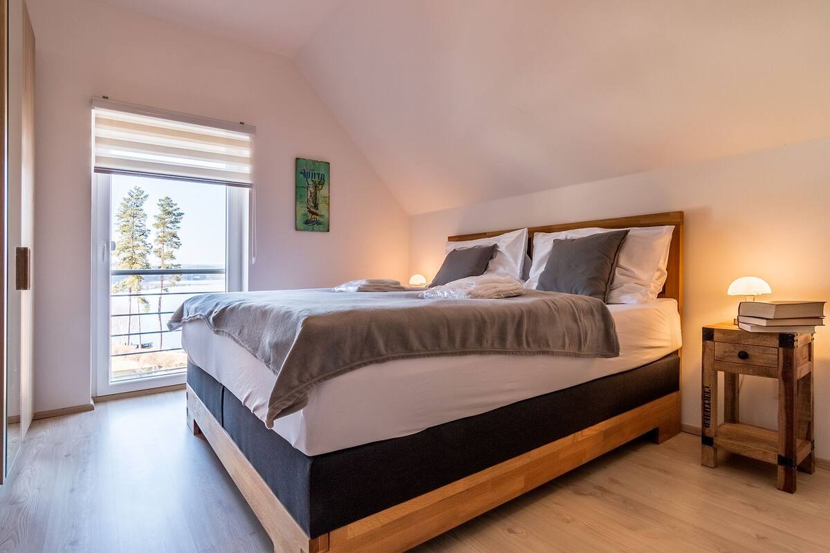 A bedroom with a bed, bedside lamps, a nightstand, and a window with blinds.