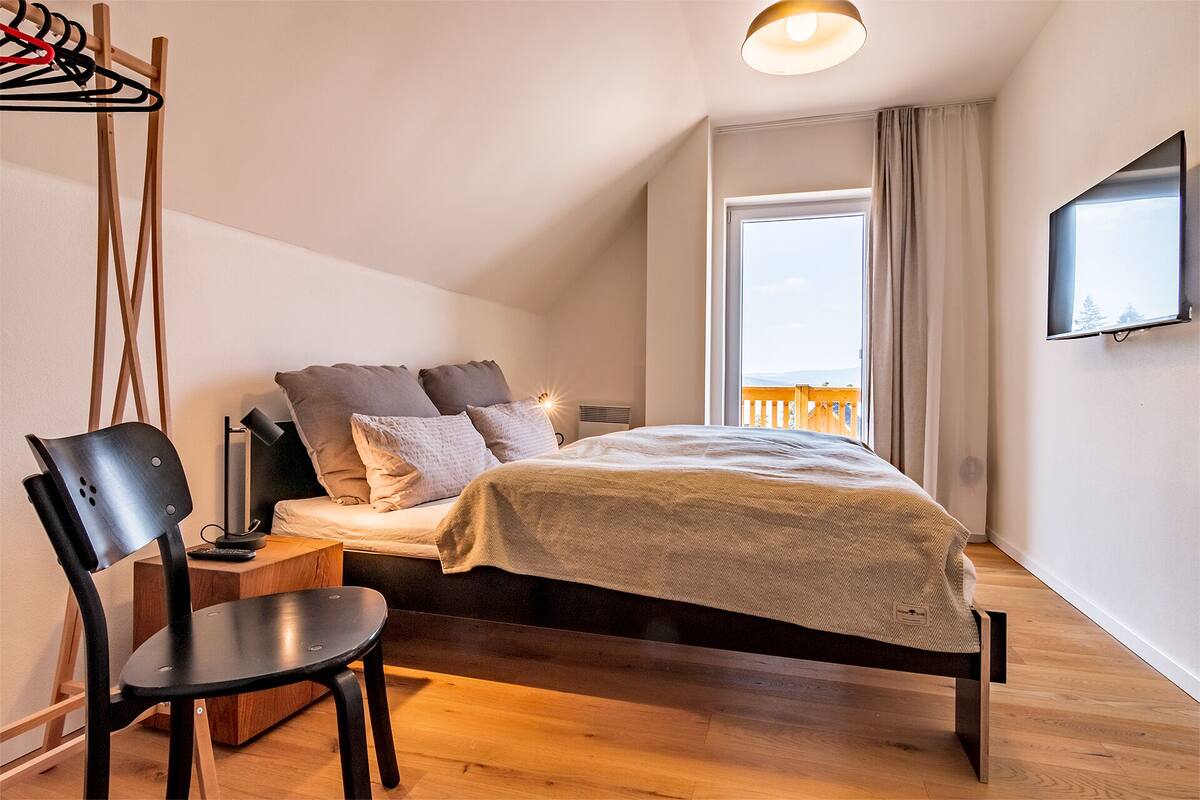 A bedroom with a bed, a chair, a desk, and a TV on the wall.