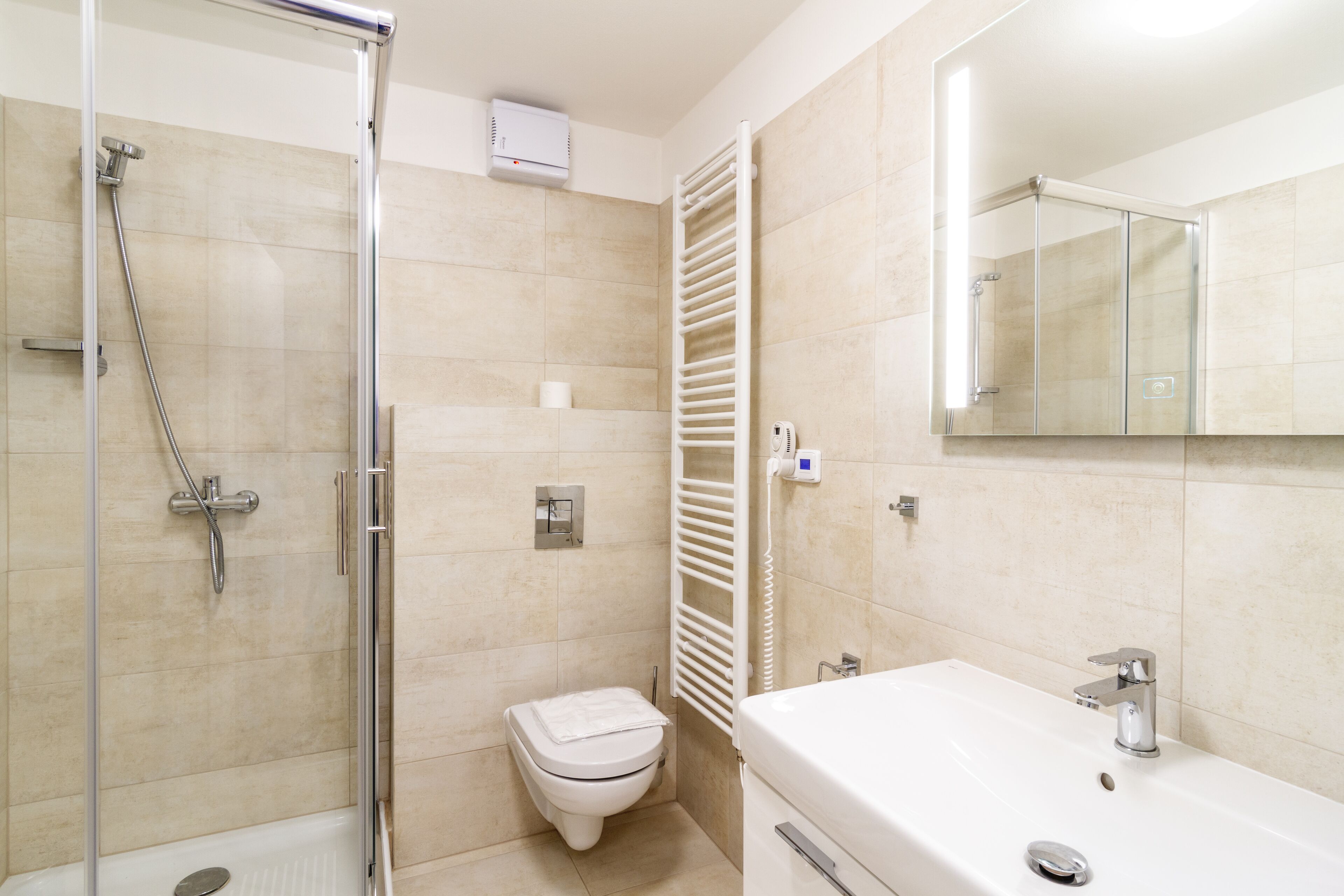 Un baño moderno con ducha de vidrio, inodoro blanco y lavamanos blanco con espejo superior.