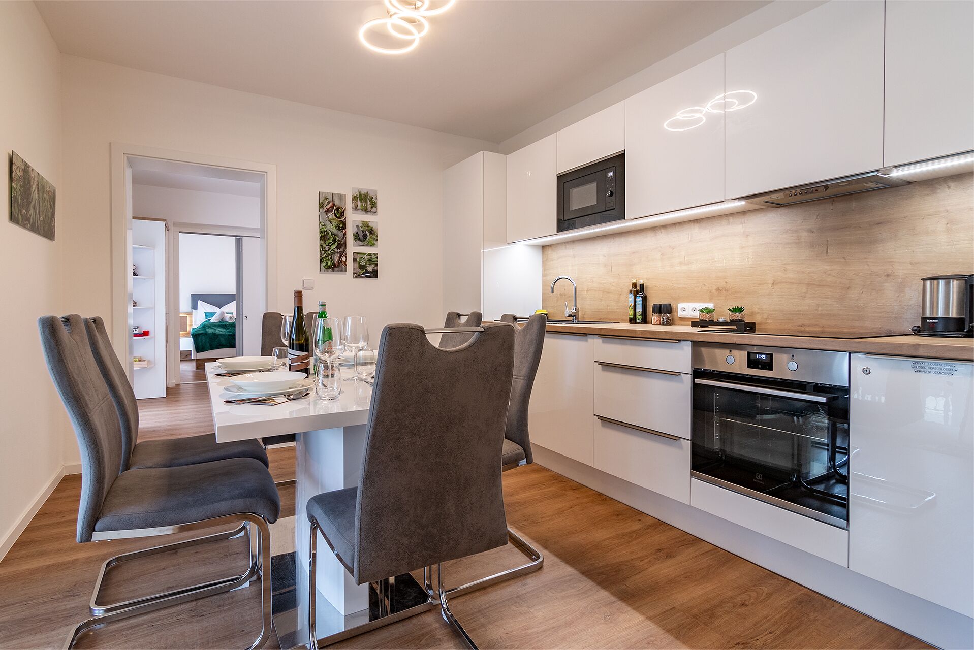 Een moderne keuken met witte kasten, een roestvrijstalen oven, en een eethoek met een tafel gedekt voor twee personen.